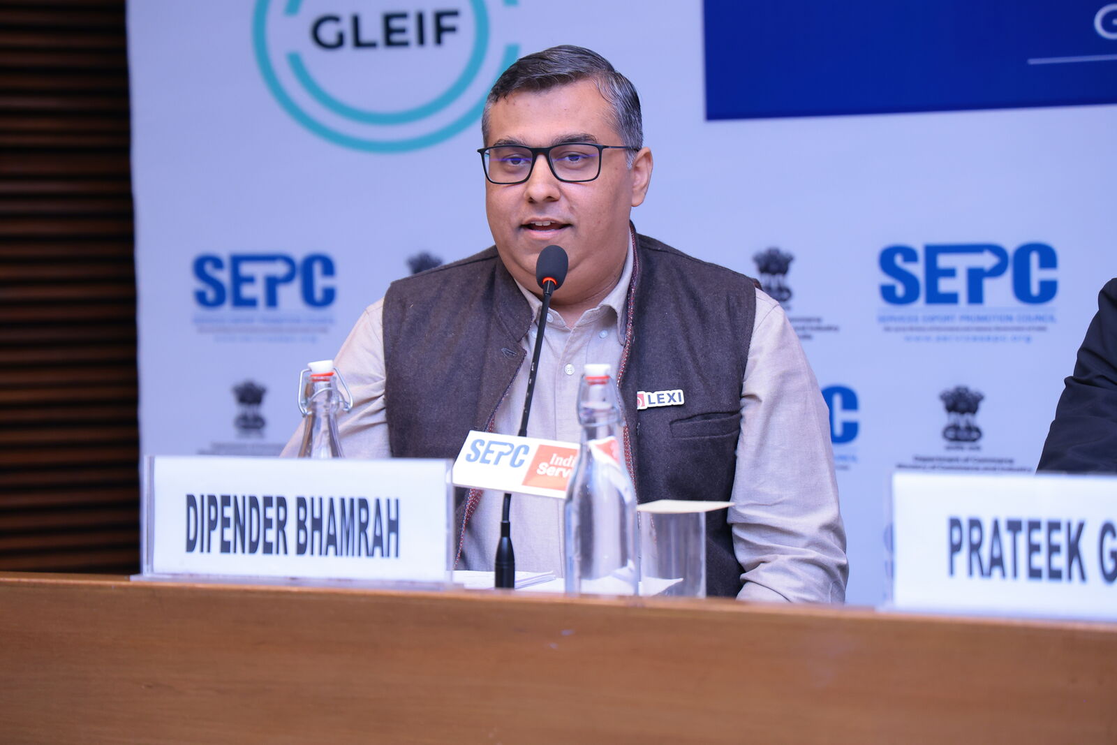 Dipender Bhamrah speaking into a microphone at the Finolegal Convergence Summit, with SEPC banners behind him