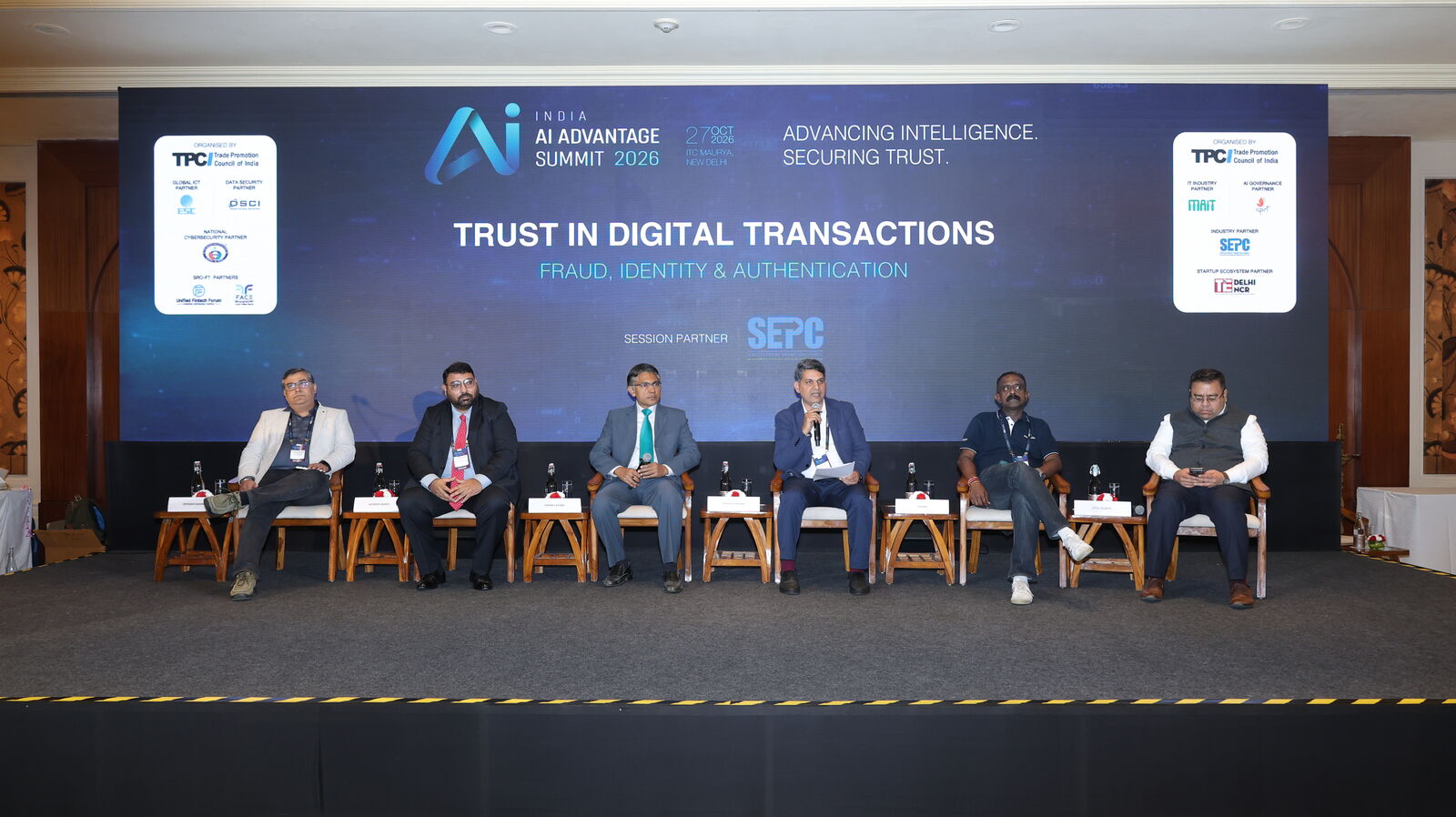 Seven panellists seated on stage under the Trust in Digital Transactions: Fraud, Identity & Authentication backdrop at the India AI Advantage Summit 2026, New Delhi